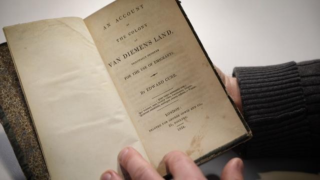 Hands hold open a book with title page "An Account of the Colony of Van Diemen's Land"