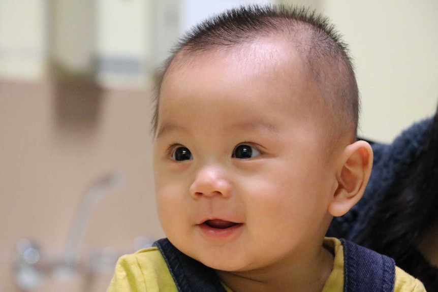 A baby wearing a yellow shirt and overalls