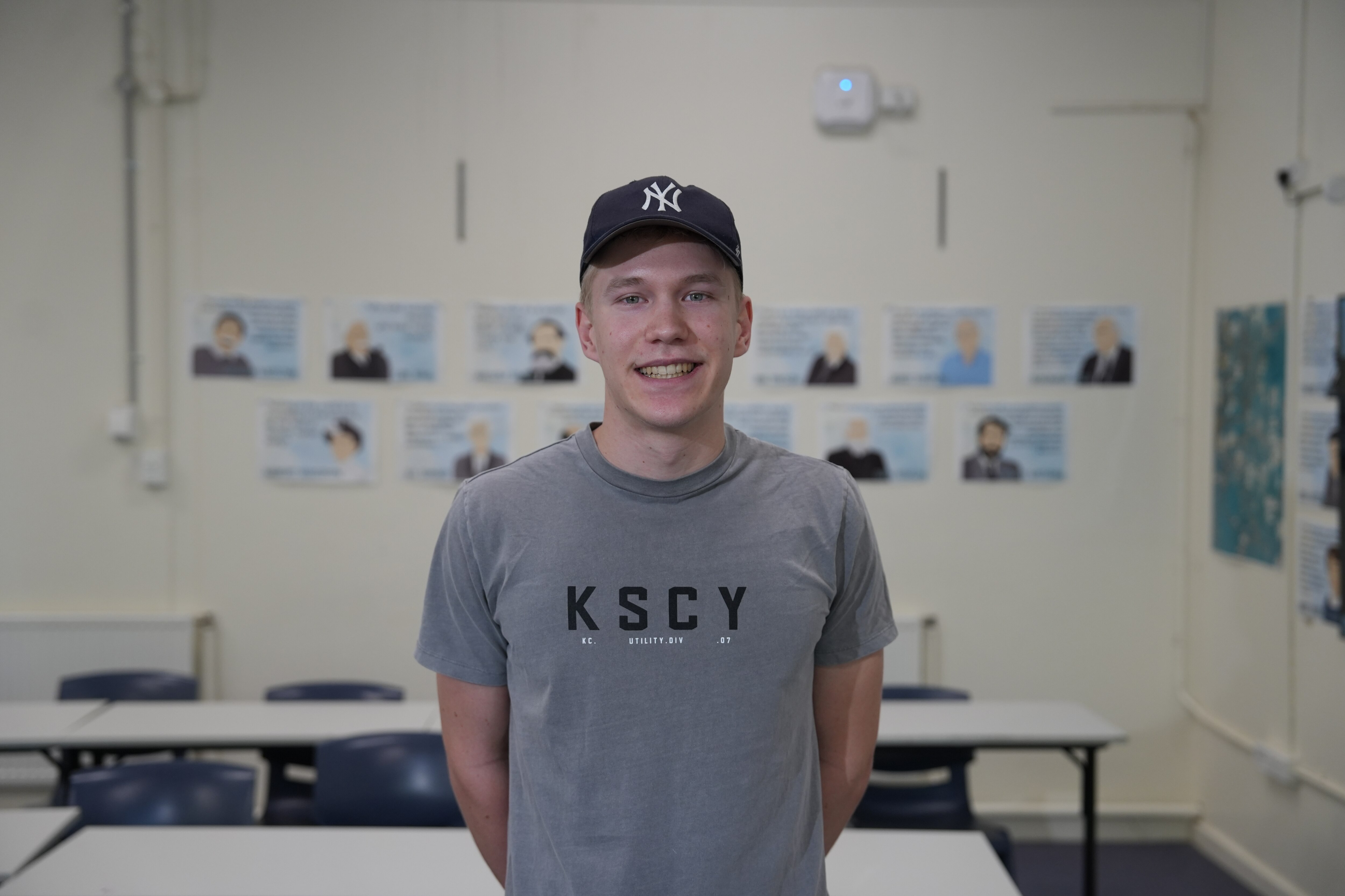 A high school aged boy in a grey t-shirt and navy New York Yankees cap smiles.
