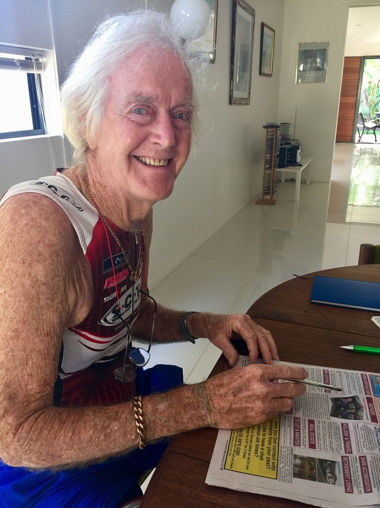 Older man sits smiling looking at a newspaper where the dating section is.
