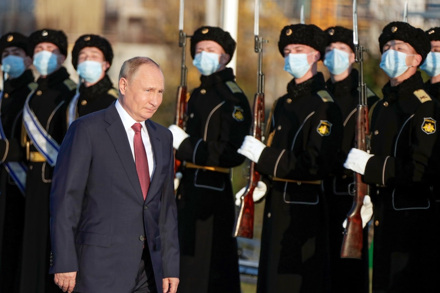 Man in a suit walks past a guard of soliders.