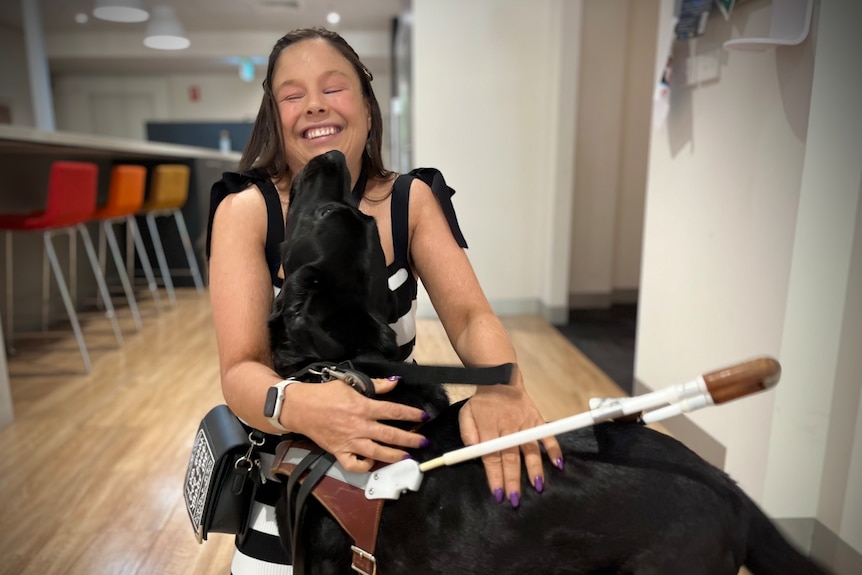 Lizzie Eastham smiles as a black dog licks her face.