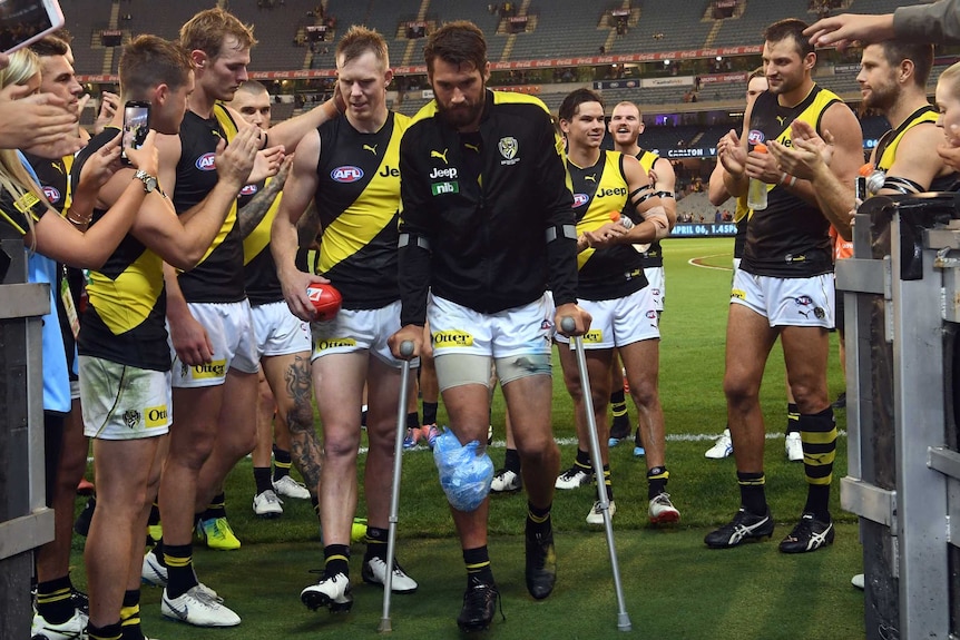 Alex Rance, on crutches with ice on his knee, leads his team off the field.