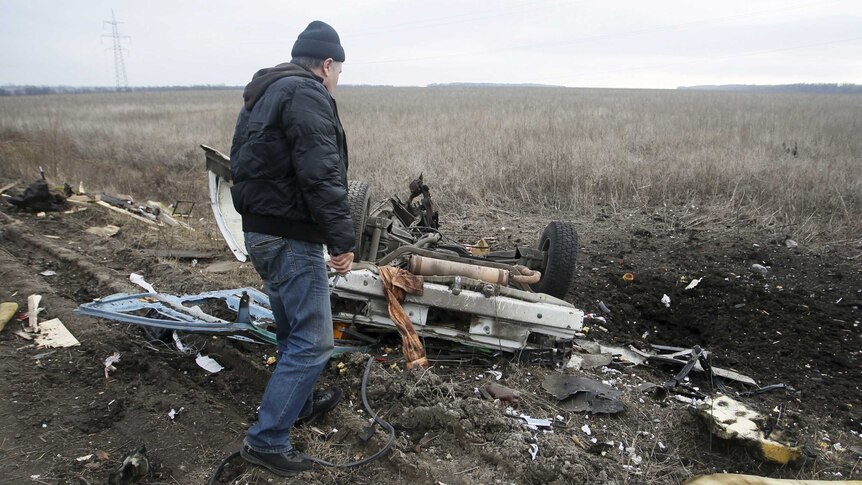 A man looks at the wreckage of an exploded minivan.