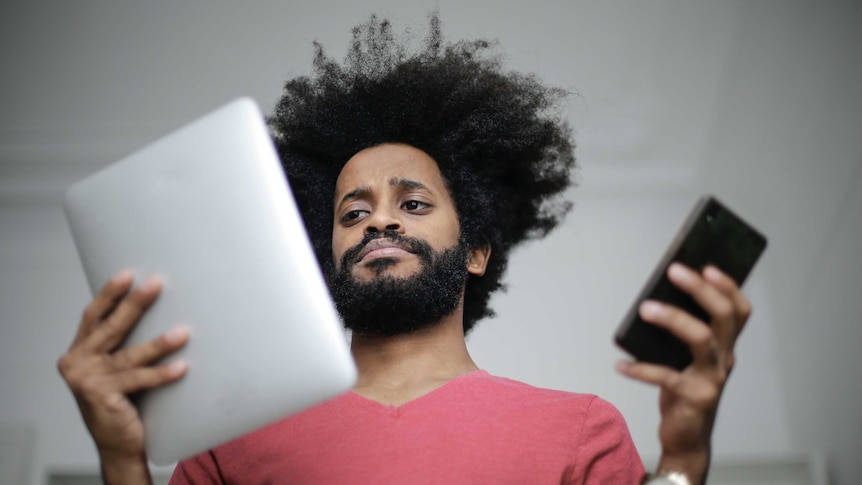 Man holding a tablet and a phone looking confused in story about how chain mail has changed and why people still send it.