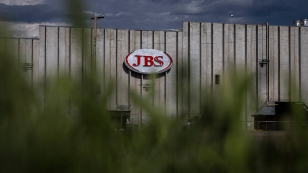 A JBS processing plant can be seen through trees. The meat company was hit by a ransomware attack