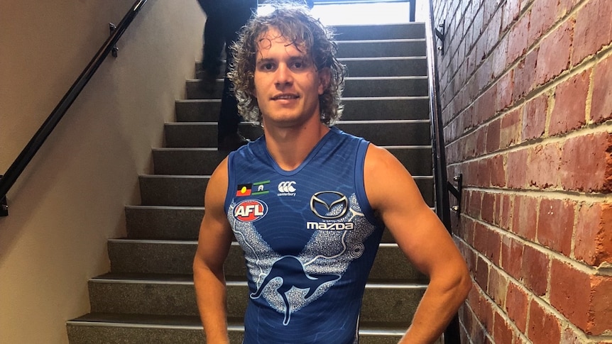 A footballer in a blue uniform stands on some stairs.