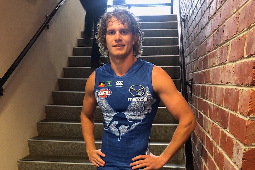 A footballer in a blue uniform stands on some stairs.