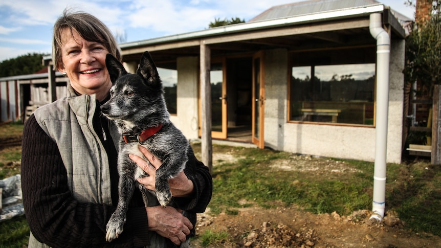 Lyn Stephenson holding her dog Eddie out the back of her 1890s cottage that has been retrofitted with hemp-lime walling.