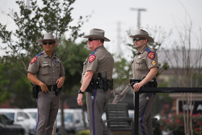 Three US police officers standing wearing beige-grey uniforms with cowboy hats.