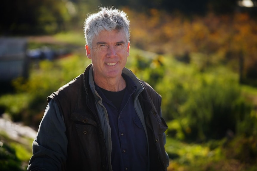 A man with grey hair and a navy shirt stands outside.