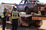 NT Police crash investigators stand next to a tow truck, with the Finke Desert Race vehicle loaded onboard.