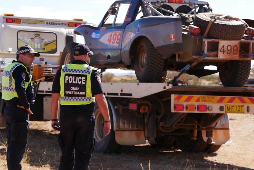 NT Police crash investigators stand next to a tow truck, with the Finke Desert Race vehicle loaded onboard.