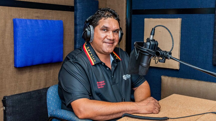 An Aboriginal man sits in a recording studio. He is wearing headphones and there is a microphone in front of him.