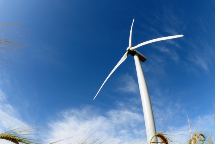 A large, white wind turbine, shot from the ground up, with a deep blue sky in the background 