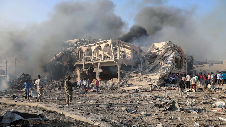 A general view shows the scene of an explosion in Mogadishu. There is smoke and a two-storey building has been reduced to rubble