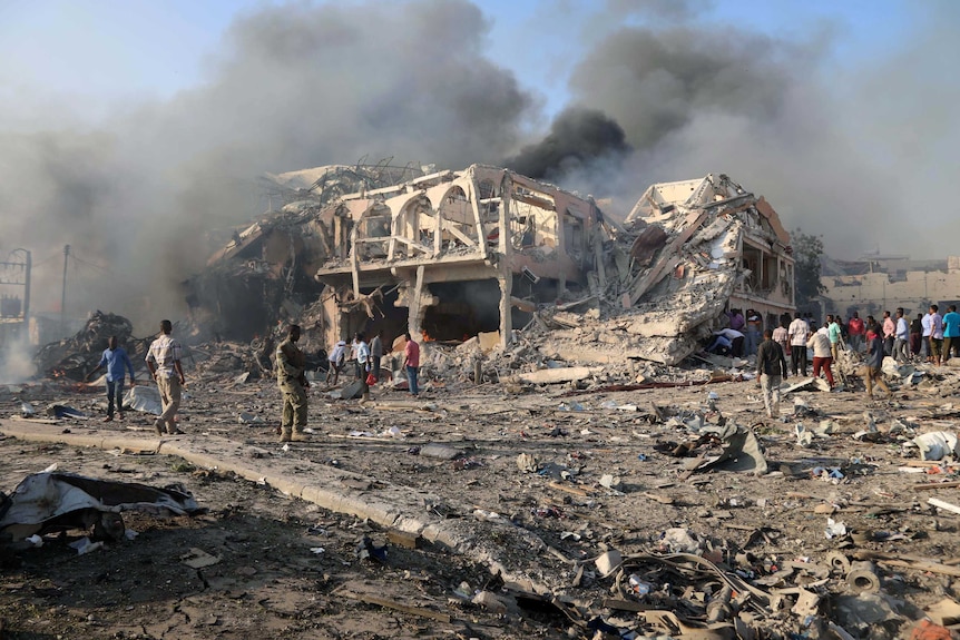 A general view shows the scene of an explosion in Mogadishu. There is smoke and a two-storey building has been reduced to rubble