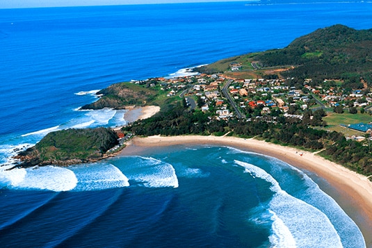 Drone image of Scott's Head community right on the beach with people surfing waves.