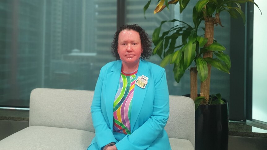A woman wearing a bright blue blazer, sitting on a couch