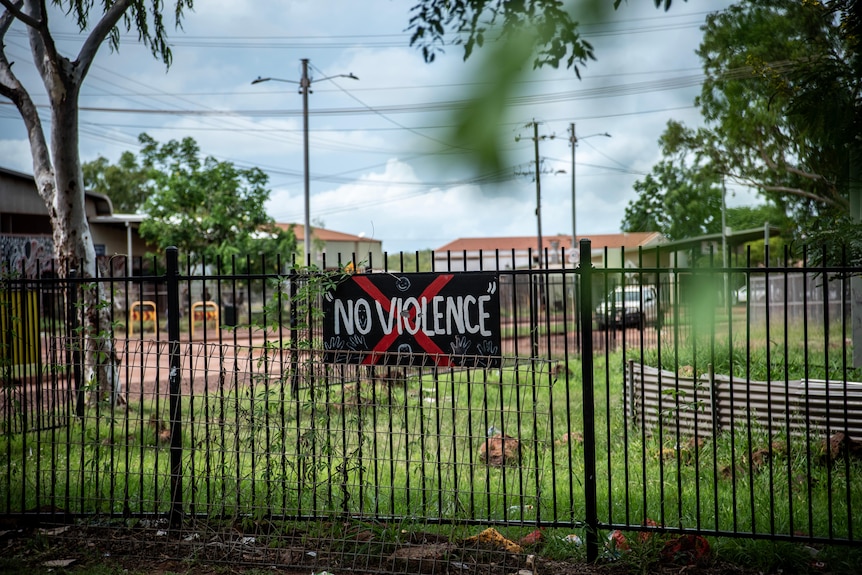 A sign depicting the words 'no violence' is hung on a fence. 