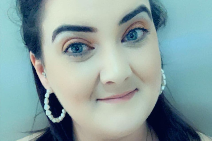 A woman wearing white hooped earrings smiles at the camera