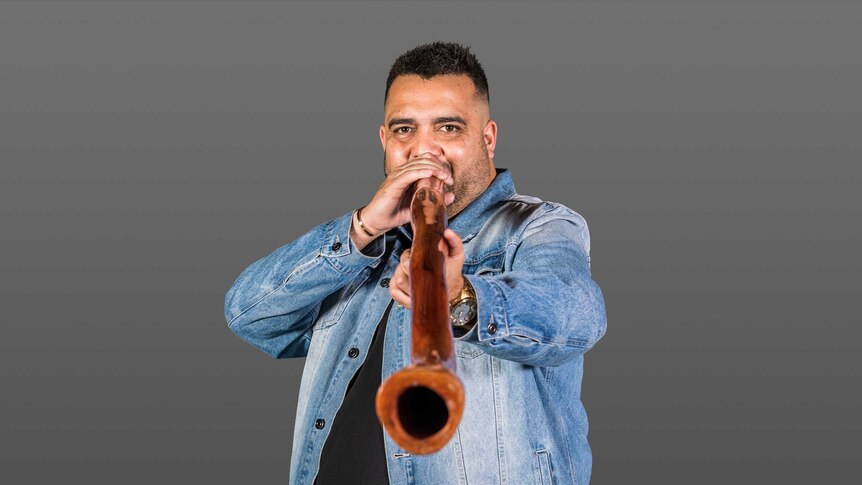 Gamilaraay comedian Dane Simpson holds Digeridoo to mouth and points it towards you