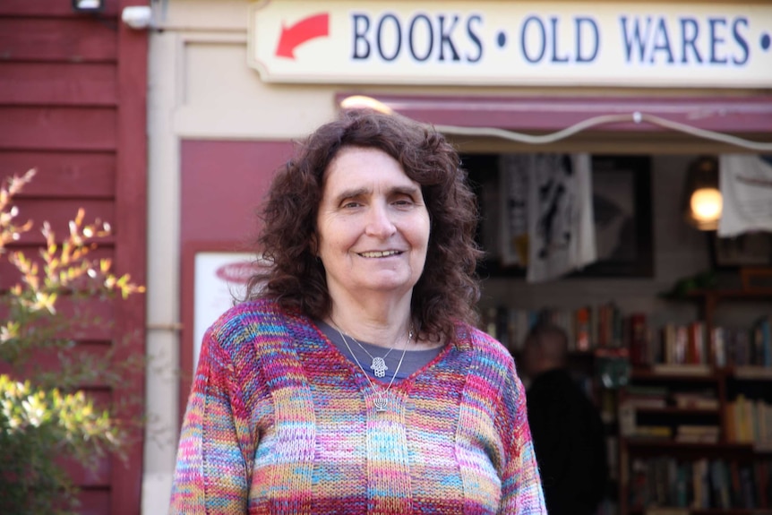 Middle-aged woman with dark brown hair standing in front of country bookstore.