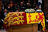 A crown sits on a coffin draped in a red and yellow flag.
