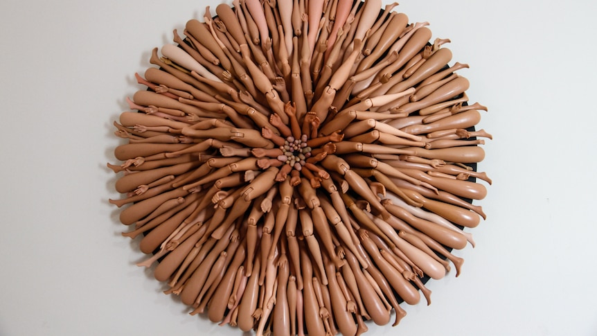 An artwork made from Barbie limbs hangs on the wall