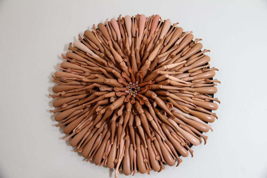 An artwork made from Barbie limbs hangs on the wall.