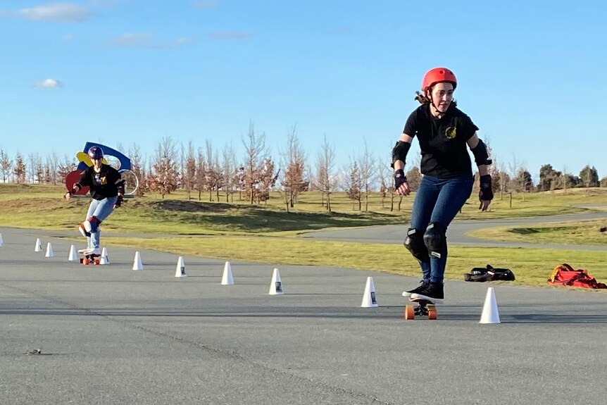 Two people on skateboards wearing helmets move around cones