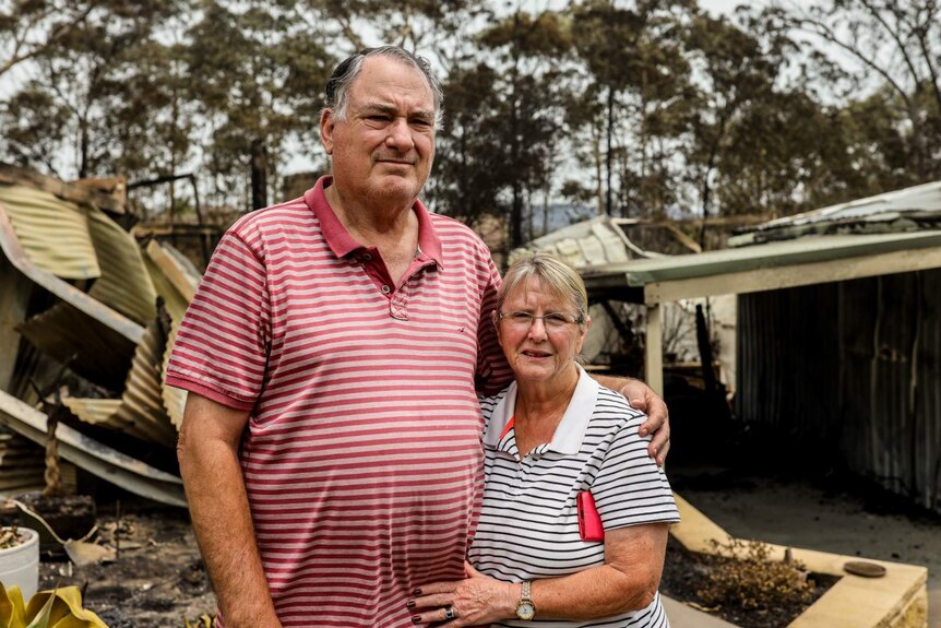 man and woman standing in front of fire ruined homes