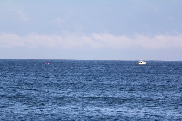 A boat in the distance in the water off Mindarie, with two orange buoys to the left.
