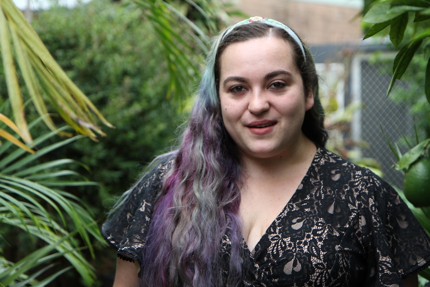 A woman with blue and purple in her hair outside in a garden looking at the camera