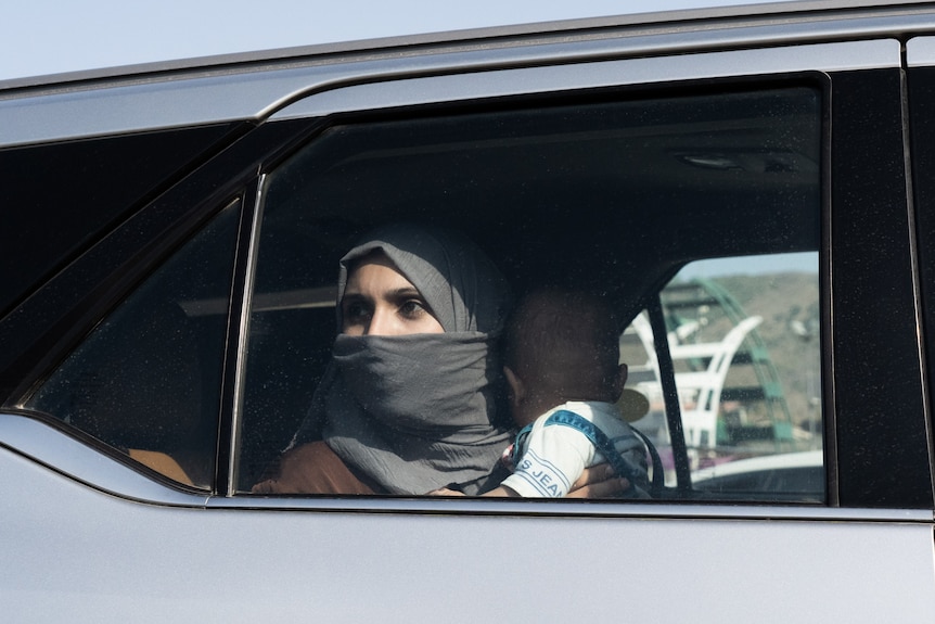A woman in a headscarf holds a baby while looking out the window of a car 