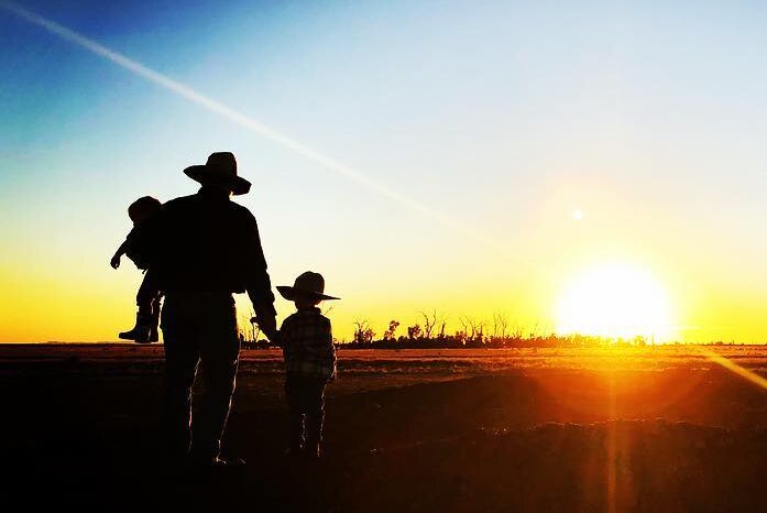 Silhouette of man and two children walking into sunset.