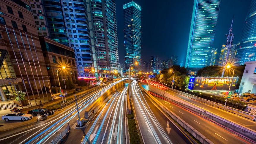 Car headlights create lines of light on road into a busy city.