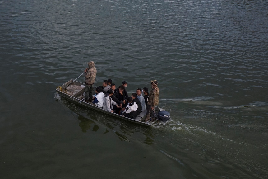 A small boat full of migrants from China crosses the Rio Grande, accompanied by army national guardsmen.