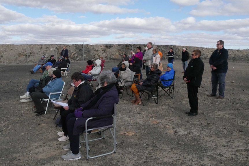 Crowd of people sitting and standing outside in the wind atop Broken Hill's Line of Lode.