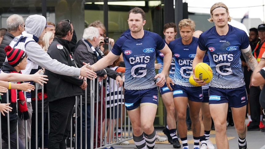 An AFL star runs out slapping hands with fans as he leads his team out before a pre-season game.