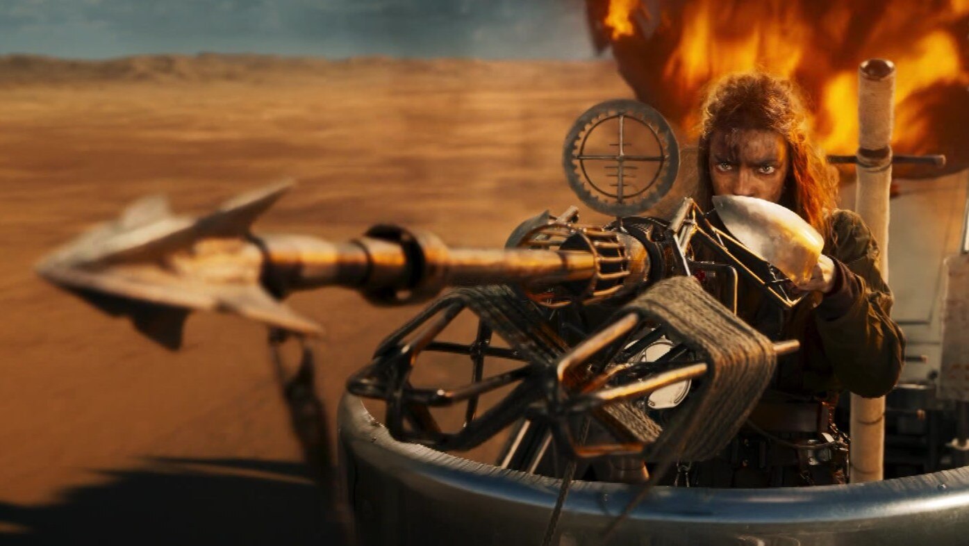 Actor Anya Taylor-Joy as Furiosa. She is pointing a crossbow, about to shoot. An explosion is going off behind her.