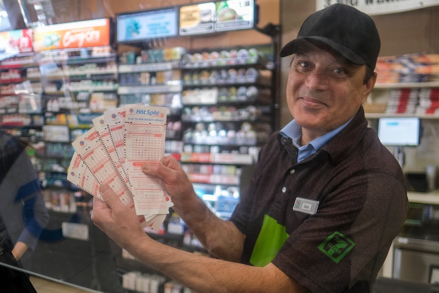 A man smiling while holding a number of lottery tickets inside a convenience store.