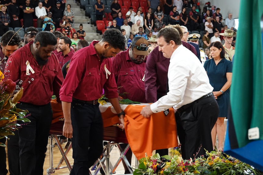 Pallbearers moving a casket with the NT flag draped over it.