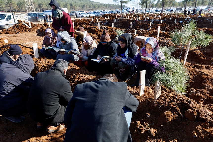 People read Koran next to graves of victims of the deadly earthquake.