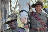Man and woman in vintage military uniform stand in front of a horse