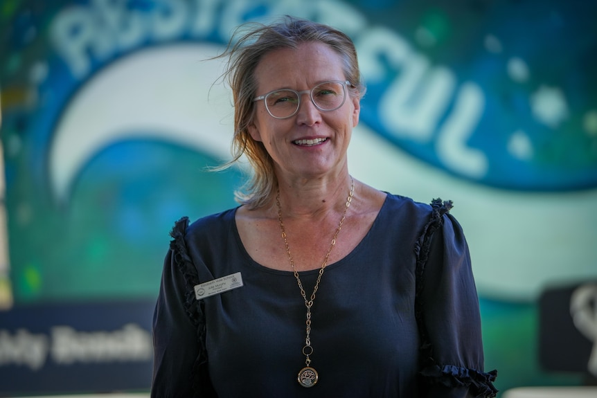 Woman wearing a blue top standing in front of a school mural.