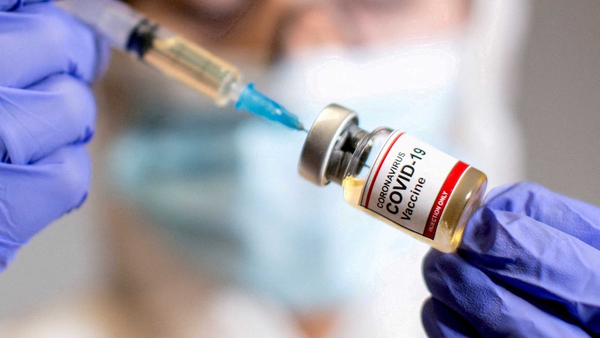 A woman holds a medical syringe and a small bottle labelled "Coronavirus COVID-19 vaccine".