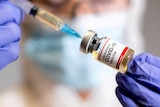 A woman holds a medical syringe and a small bottle labelled "Coronavirus COVID-19 vaccine".