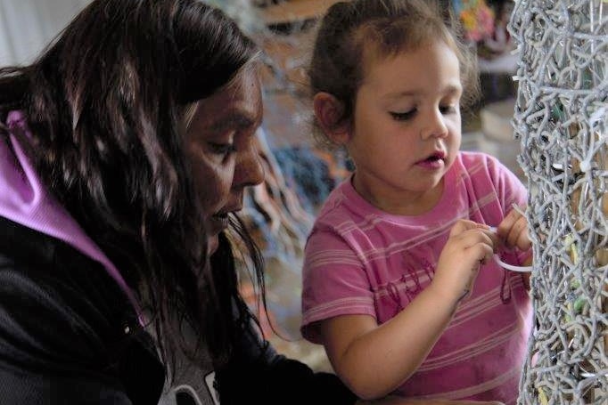 First Nation's women on right helping young granddaughter weaving netting.