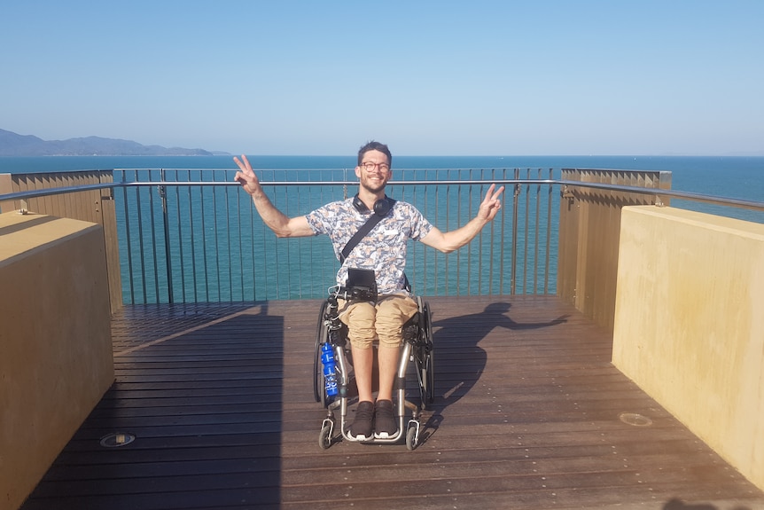A man in a wheelchair poses and smiles at a lookout over the ocean